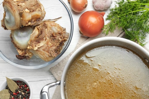 Preview: Delicious homemade bone broth and ingredients on white wooden table, flat lay