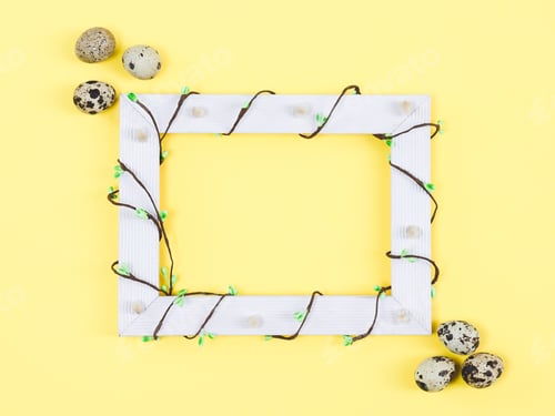 Preview: An empty wooden frame entwined with a branch with green buds and quail eggs on a yellow background.