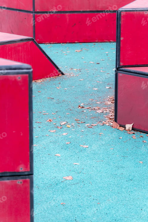Preview: Blue rubber playground with red bars and fallen leaves: Active outdoor fun among triangular shapes.