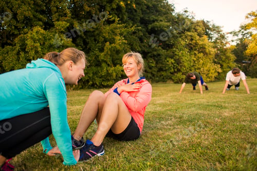 Preview: Happy sporty woman helping sister in doing stretching exercise at park