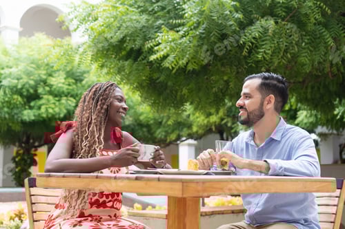 Preview: Happy multi-ethnic couple enjoying coffee and pastry at outdoor cafe
