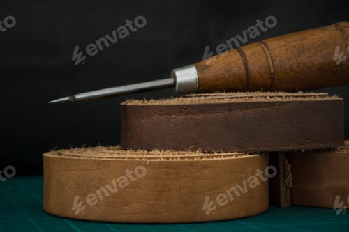 Preview: Closeup shot of a wooden stitching awl and genuine leather rolls on a craftsman's work table