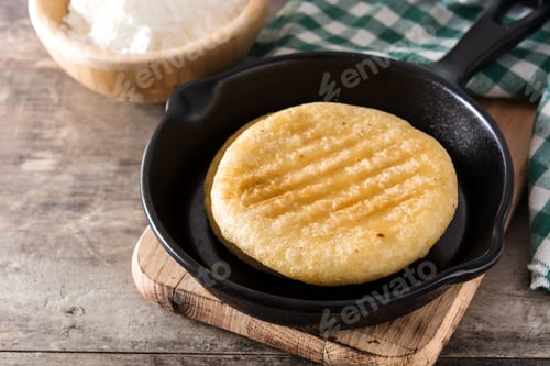Preview: Cooking arepa in frying pan with precooked corn flour on rustic wooden table