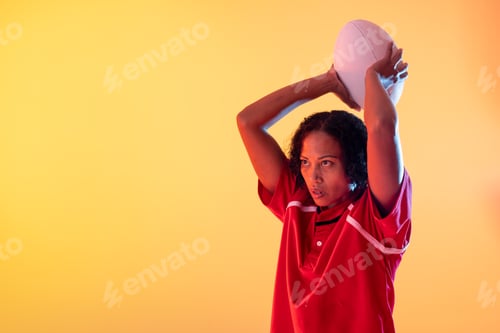 Preview: African american female rugby player with rugby ball over neon yellow lighting