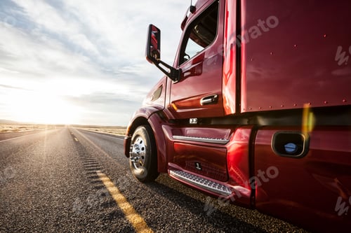 Preview: Close up side view looking forward of a commercial truck on a highway at sunset.