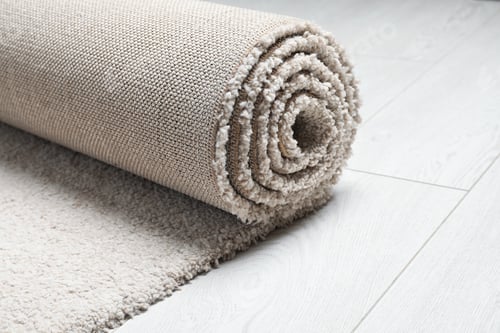 Preview: Rolled fuzzy carpet on wooden background, closeup. Space for text