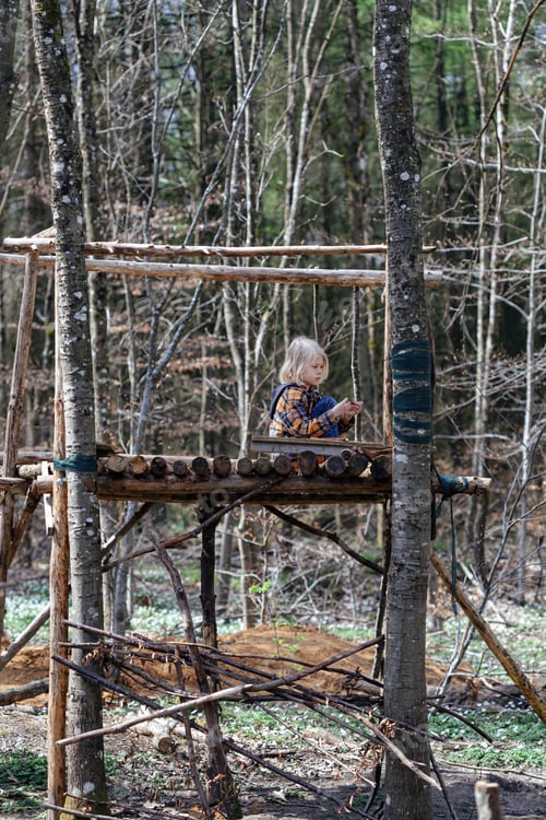Preview: A blonde child is playing in the forest in a fort built by scouts