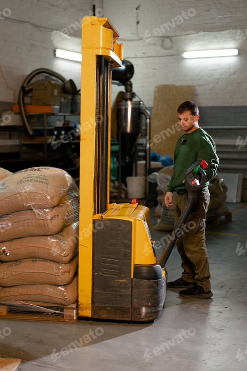 Preview: a worker at coffee factory uses a yellow forklift to lower bags of coffee