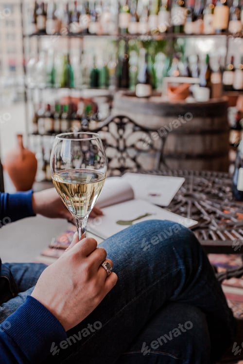 Vorschau: Hand, die ein Glas Wein hält, während man ein Buch liest