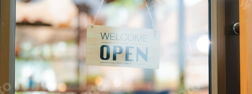 Preview: Hand of coffee shop staff woman wearing apron turning open sign board on glass door