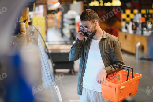 Preview: Handsome man shopping in supermarket, smilling, using phone.