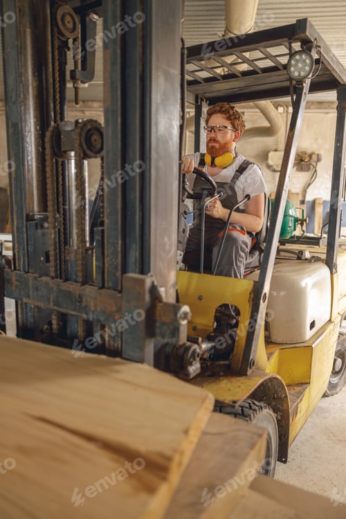 Preview: Male craftsman at wooden sawmill warehouse is loading with loader wooden board. High quality photo
