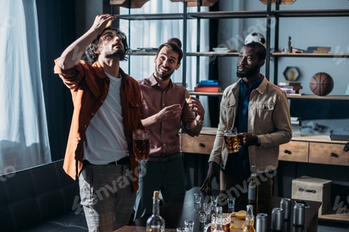 Preview: young multiethnic male friends drinking beer and partying together