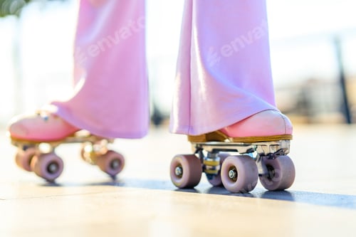 Preview: close up photo of legs woman in bell-bottomed trousers with pink pastel color roller skates outdoors