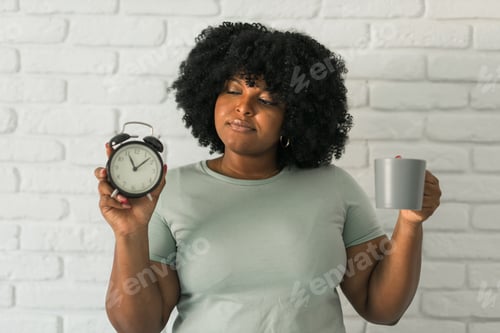 Preview: Happy african american woman holding alarm clock amazed with open mouth and surprise happy face at