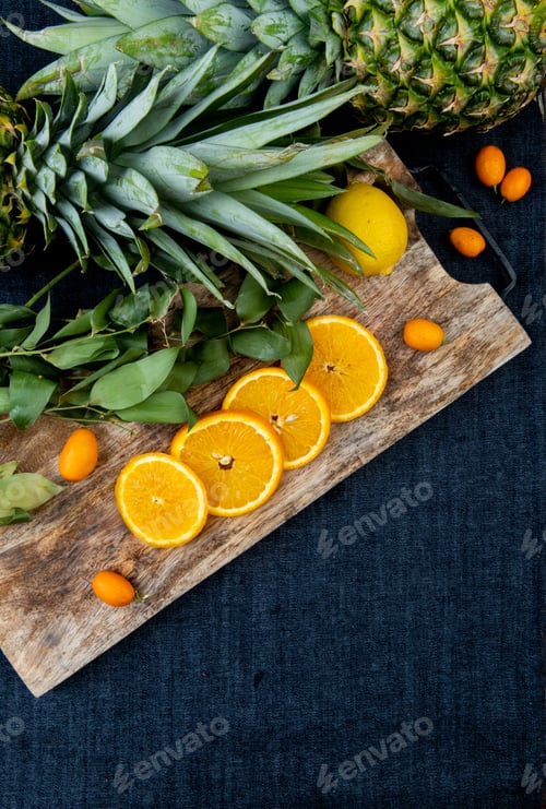 Preview: side view of citrus fruits as orange kumquat lemon on cutting board with pineapples and leaves