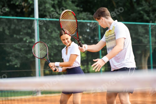 Preview: Young guy teaches a woman to play tennis. Couple with rackets in their hands on the tennis court