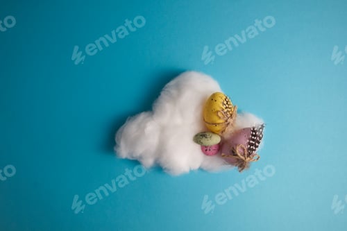 Preview: Decorated Easter eggs and colored candies on a cloud of cotton wool on a blue background