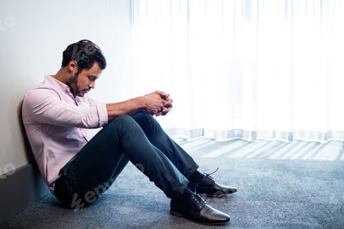 Preview: Depressed businessman sitting against a wall and looking down