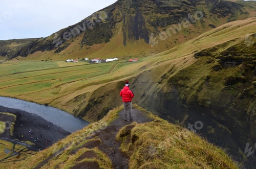 Preview: Man in a red jacket standing at the edge of a cliff landing looking out