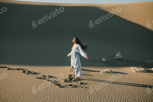 Preview: Woman with long hair in a stylish dress poses in the desert sands.