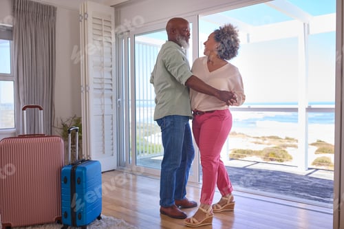 Preview: Mature Couple With Luggage Dancing In Beachfront House Overlooking Ocean For Summer Vacation