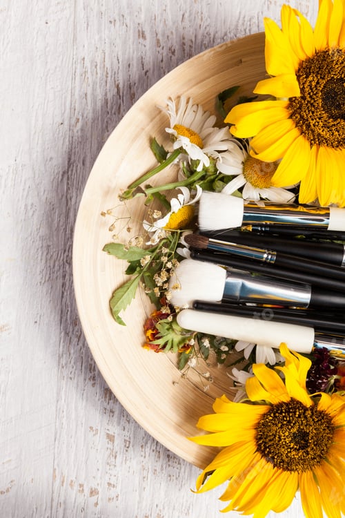 Preview: Different Make up brushes on plate next to wild flowers