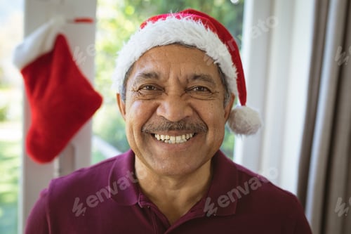 Preview: Portrait of happy biracial senior man in santa hat at christmas