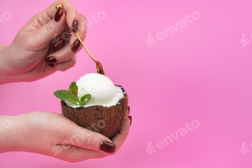 Preview: Vanilla ice cream balls in a fresh coconut half, decorated with mint leaves in the hand with a spoon