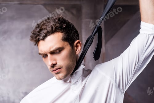 Preview: Taking his necktie away. Tired young man in formalwear taking off his necktie and looking away