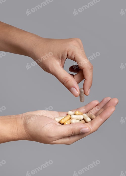 Preview: Female hand taking one beige medical capsule and holding others in cupped hand against grey