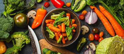Preview: Steamed carrot broccoli salad in bowl and assorted cut fresh vegetables on rustic concrete table