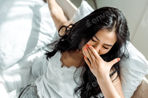 Preview: overhead view of asian woman with closed eyes covering face with yawning
