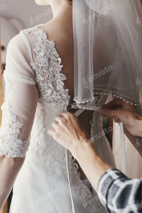 Preview: Mother hands holding ribbons and helping dressing beautiful bride in morning