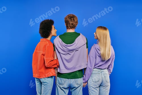 Preview: polygamy, back view of polyamory three people, young man and multicultural women holding hands