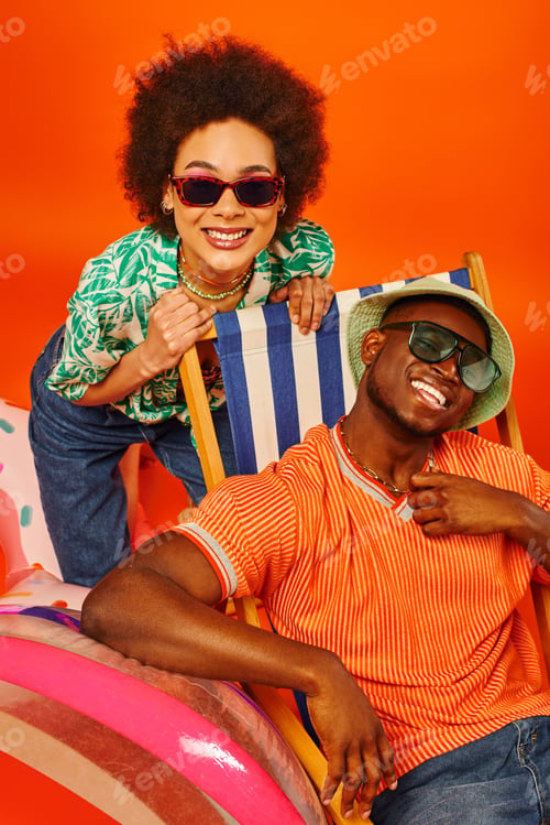 Preview: Positive young african american woman in sunglasses and summer outfit standing near best friend