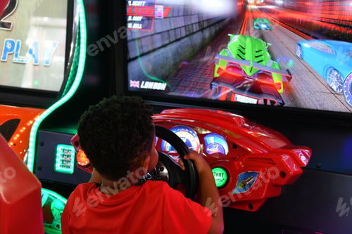Preview: Small African-American boy playing a race car driving game in an arcade.