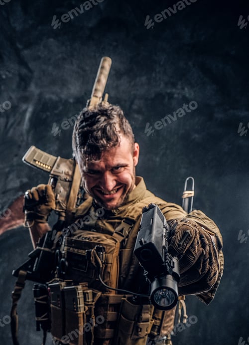 Preview: Crazy special forces soldier in body armor holding assault rifle and aiming a gun at the camera