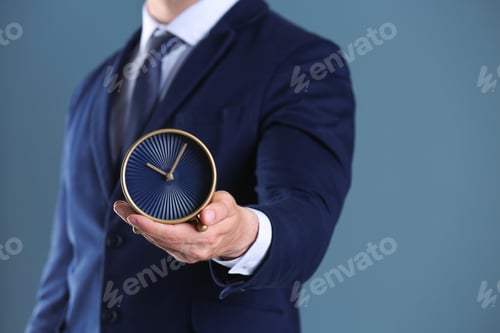 Preview: Businessman holding alarm clock on color background. Time concept