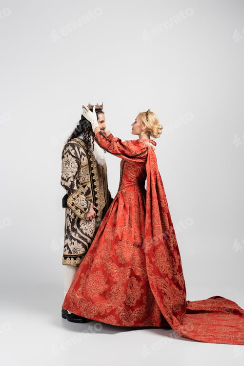 Preview: full length of blonde queen in dress wearing crown on hispanic king in medieval clothing on white