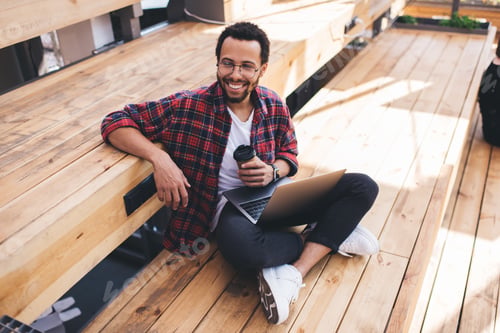 Preview: Happy male IT professional with netbook and takeaway cup enjoying freelance lifestyle