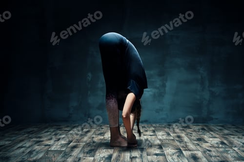 Preview: Young woman doing yoga standing forward bend pose in dark room