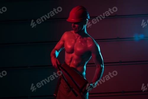 Preview: sexy shirtless fireman in protective helmet holding fire extinguisher in darkness