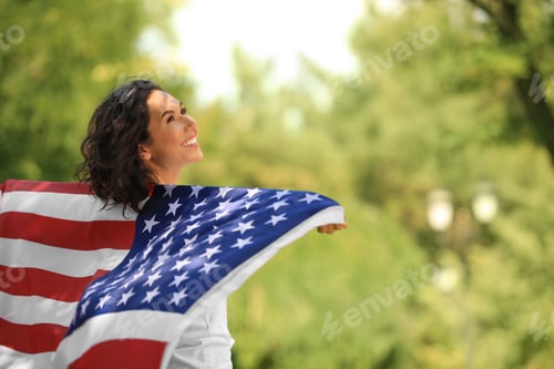 Preview: Happy young woman with American flag in park on sunny day