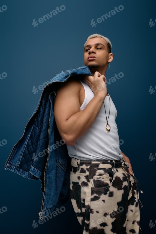 Preview: Stylish young black man showcases denim jacket against a bold blue backdrop