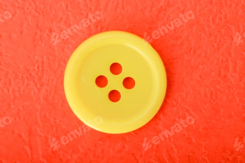 Preview: Yellow sewing button isolated on a red background.