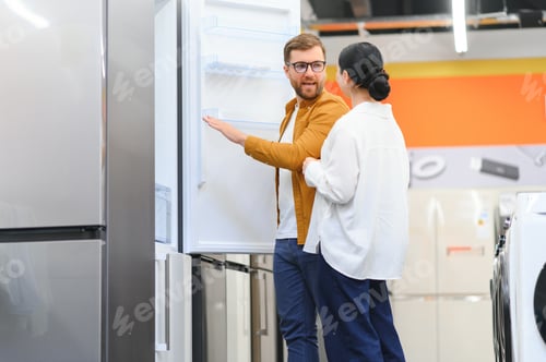 Preview: family couple buying domestic refrigerator in supermarket