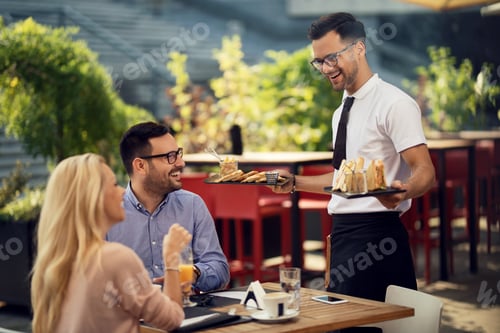 Preview: Happy waiter serving lunch to a couple in a restaurant.
