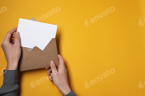 Preview: Woman taking card out of letter envelope at orange table, top view. Space for text
