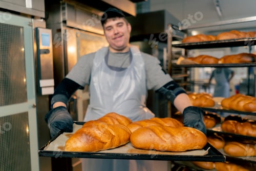 Preview: close up In a professional kitchen an inclusive baker stands with ready-made bread on a tray smiling